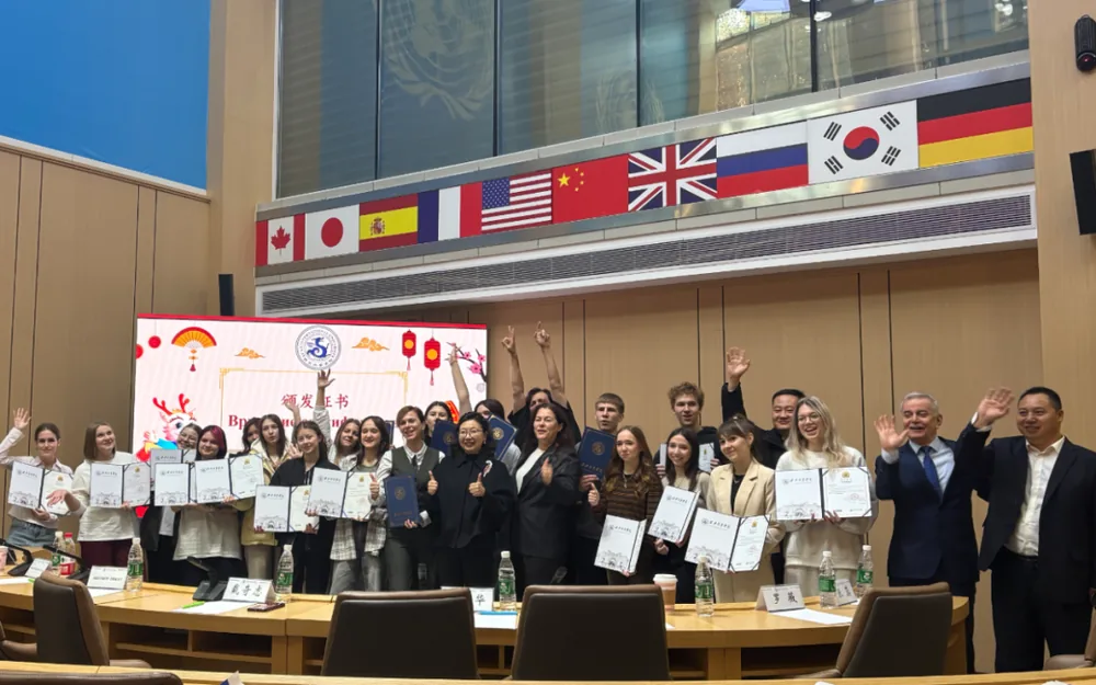 A certificate presentation in a meeting room hung with international flags