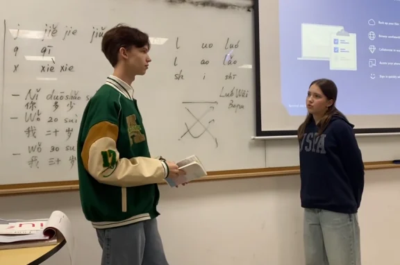 Two students at a whiteboard with Chinese pinyin written on it