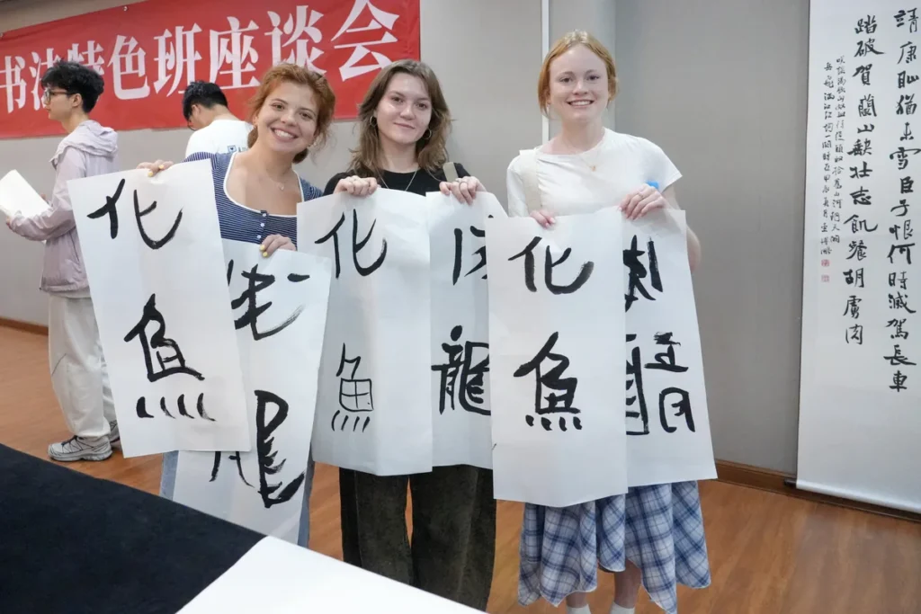 Three students holding up their calligraphy in front of a banner